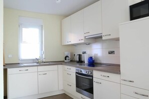 A modern kitchen with white cabinets, a stainless steel oven, and a window providing natural light. - Holiday home in Wittmund with swimming pool (Wittmund)