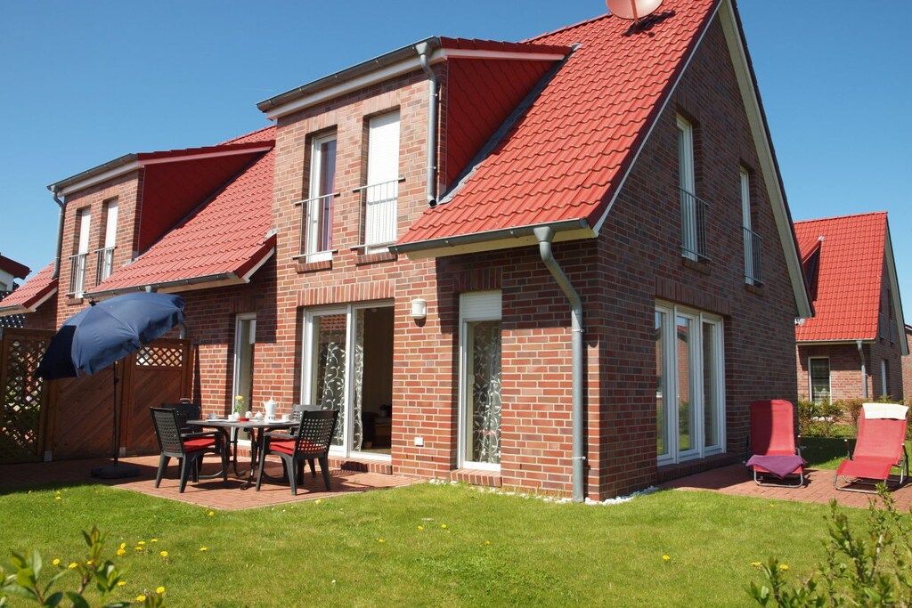 Een twee verdiepingen tellend bakstenen huis met een rood dak, een terras met tafel en stoelen, en een tuin.