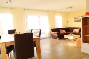 A living room with a sofa, a dining table with chairs, and a coffee table. - Holiday home in Wittmund with swimming pool (Wittmund)