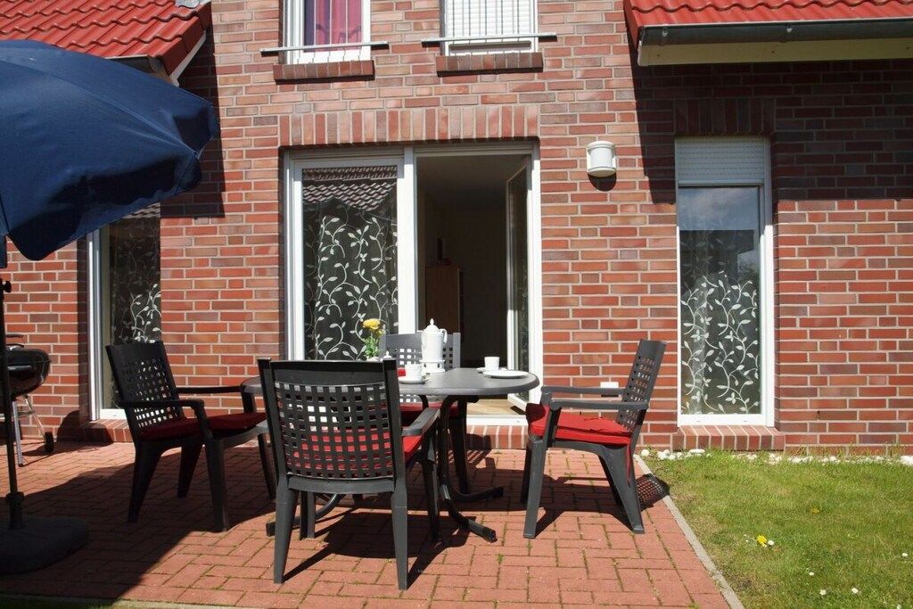 An outdoor patio with a brick wall, a table with chairs, and a blue umbrella.
