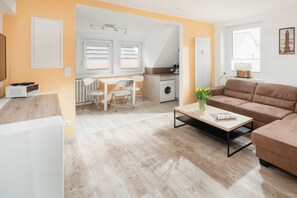 A modern living room with a sofa, a coffee table, and a dining area with chairs and a table. - Holiday apartment with 1 bedroom (Norderney)