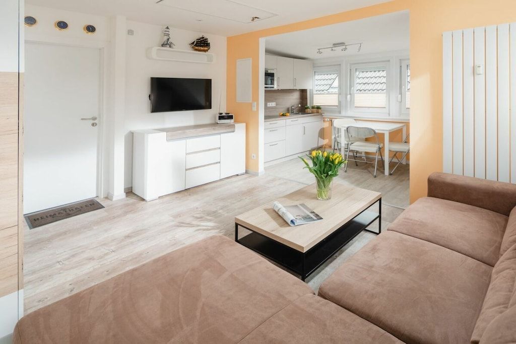 Een moderne woonkamer met een bank, een salontafel met een tijdschrift en een aan de muur bevestigde televisie.