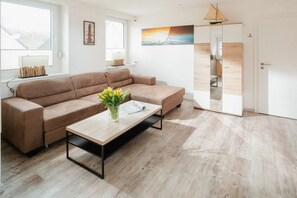 Een moderne woonkamer met een bank, een bijzettafeltje met een bloevas en een schilderij aan de muur.