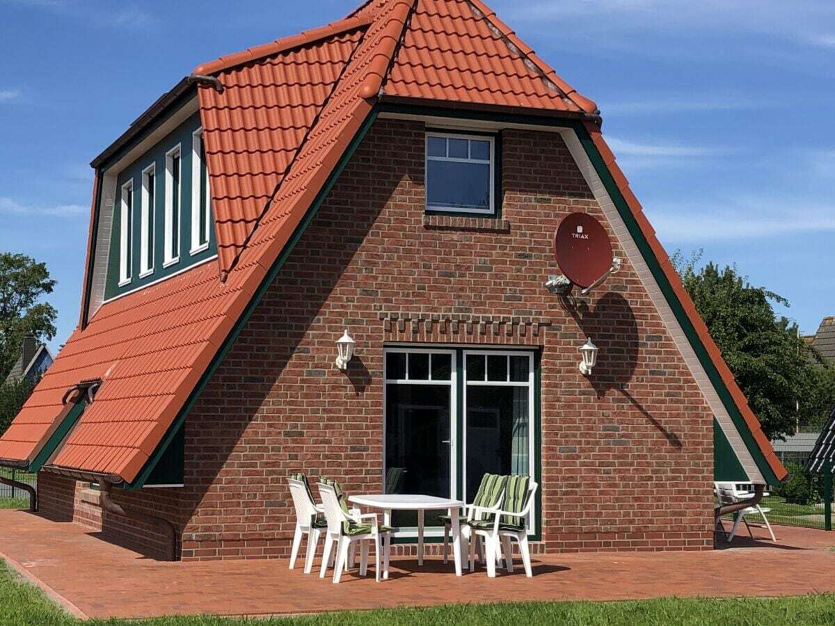 Uma casa de tijolos com telhado vermelho, uma porta da frente e um pequeno pátio com móveis de exterior.