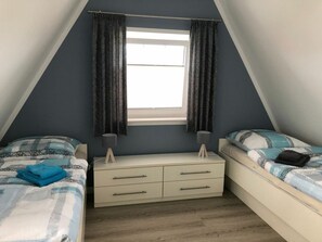 A bedroom with two beds, a dresser, and a window with curtains. - Dream Berth Boatswain (Wittmund)