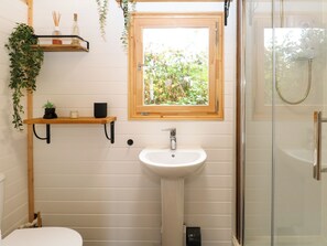 Ein Badezimmer mit einem weißen Waschbecken, einer Toilette, einer Dusche und einem Fenster mit Blick auf Grünflächen.