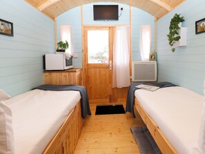 Ein Zimmer mit zwei Betten, einem Fernseher, einem kleinen Tisch mit einer Pflanze und einem Fenster mit Vorhängen.
