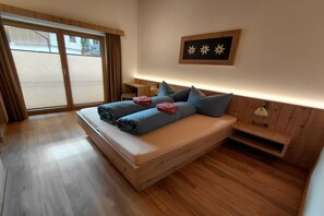 A bedroom with a bed, a bedside table, a lamp, and a window with curtains. - Modern holiday apartment in a quiet location (Längenfeld)