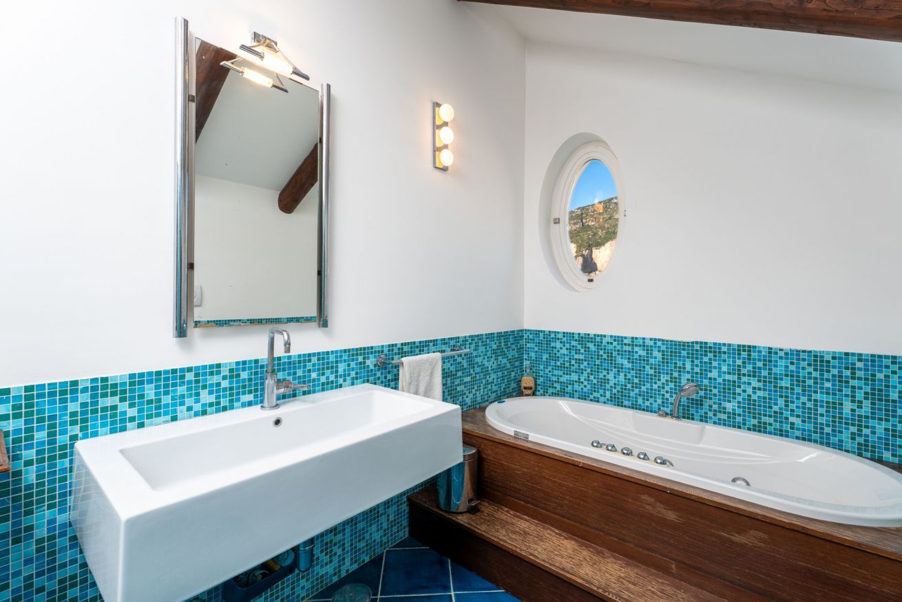 Ein Badezimmer mit einem weißen Waschbecken, einer Badewanne, einem Spiegel und einer Wandleuchte.