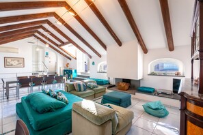 A spacious living area with a high ceiling and exposed wooden beams, a fireplace, and a dining area with modern furniture. - La Terrazza nel Blu | Sea View (Piano di Sorrento)