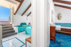 A room with a balcony, a bed with a teal bedspread, a wooden cabinet, and a bathroom with a blue-tiled floor. - La Terrazza nel Blu | Sea View (Piano di Sorrento)
