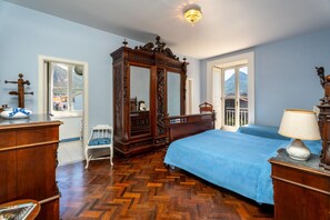 Een slaapkamer met houten vloer, een grote spiegel, een bed met een blauwe spreideken en een houten dressoir.