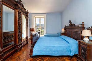 A bedroom with a large mirror, a bed with blue bedding, a wooden dresser, and a view through a window. - La Terrazza nel Blu | Sea View (Piano di Sorrento)