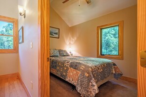 A bedroom with a bed, a nightstand, a lamp, and two windows. - Escape to 8 private acres in Floyd County with Little River views and direct private river access. Enjoy fishing, kayaking, private trails, high-speed WiFi, a dedicated workspace, a kids' area and plenty of room to relax in nature. (Floyd)