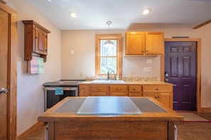 A kitchen with wooden cabinets, a central island, a window with a view of trees, and a purple door. - Escape to 8 private acres in Floyd County with Little River views and direct private river access. Enjoy fishing, kayaking, private trails, high-speed WiFi, a dedicated workspace, a kids' area and plenty of room to relax in nature. (Floyd)