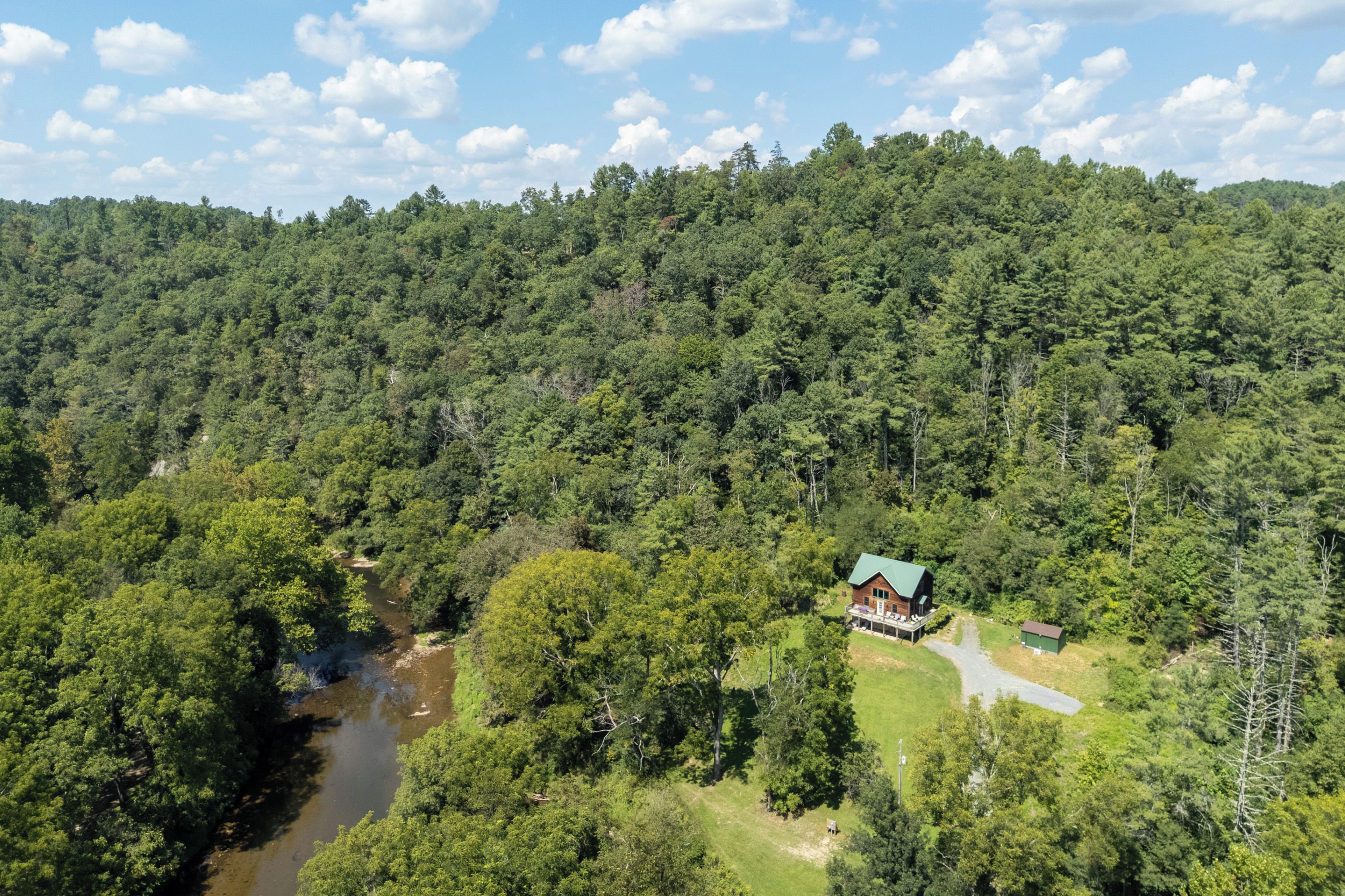 High aerial view of the cabin nestled in a lush forest clearing alongside the river.