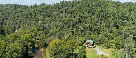 High aerial view of the cabin nestled in a lush forest clearing alongside the river.