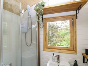 Ein Badezimmer mit Duschkabine aus Glas, einem Holzfenster und einem weißen Waschbecken.