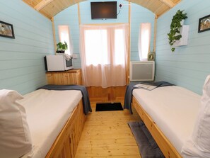 Ein Zimmer mit zwei Betten, einem Fernseher, einem kleinen Tisch mit einer Pflanze und einem Fenster mit Vorhängen.