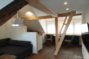 A loft-style room with a sloped ceiling, wooden beams, a desk, a chair, and a sofa. - Apartment with 1 bedroom (Zeltingen-Rachtig)