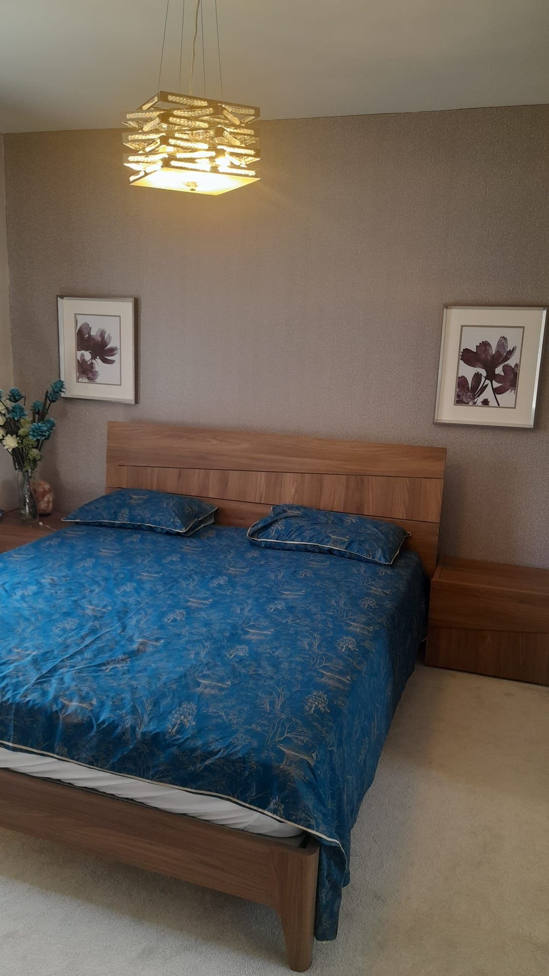 A bedroom with a wooden bed, a hanging light fixture, and two framed floral pictures on the walls.