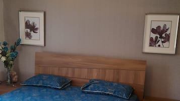 A bedroom with a wooden bed, a hanging light fixture, and two framed floral pictures on the walls.