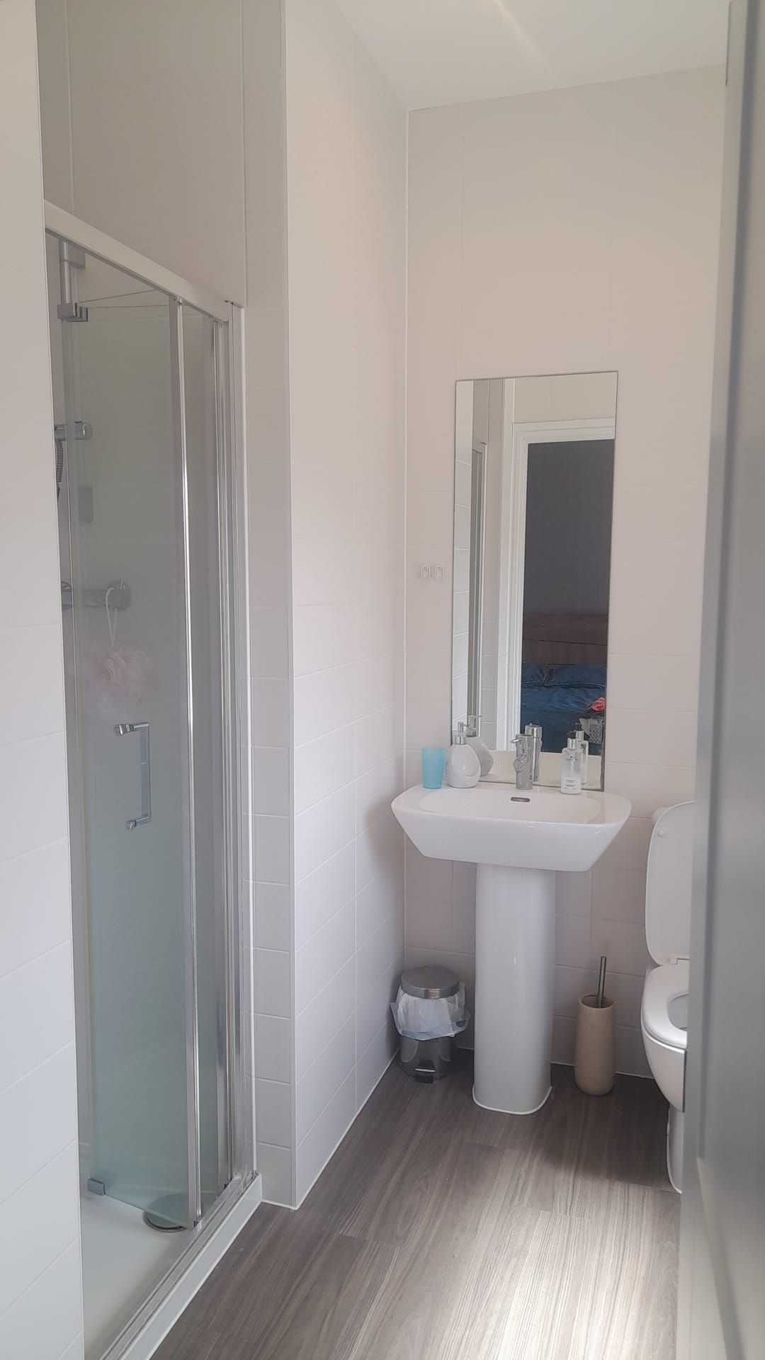 A bathroom with a glass-enclosed shower, a pedestal sink, and a toilet.