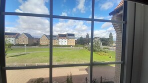 A view through a window with a clear sky, a grassy courtyard, and buildings in the background.