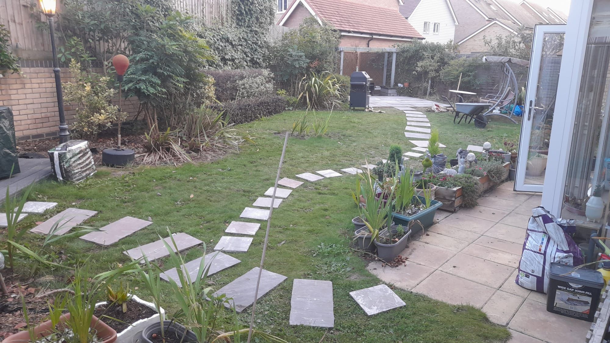 A backyard with a paved pathway, potted plants, and a barbecue area.