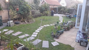 A backyard with a paved pathway, potted plants, and a barbecue area.