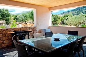 Eine Terrasse im Freien mit Glastisch und Stühlen, einer Steinmauer und Blick auf eine Berglandschaft.