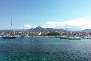 En kystnær lysthavn med fortøjede både, en klar himmel og et bjergrigt landskab i baggrunden.