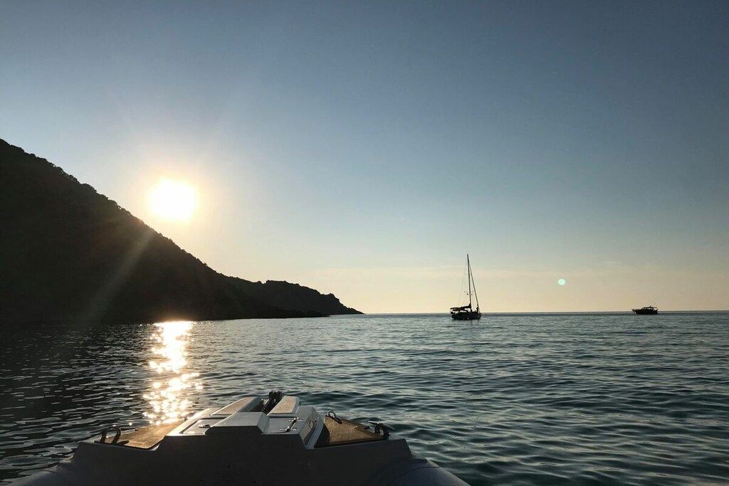 Um barco em águas calmas sob um céu claro com o sol se pondo ou nascendo no horizonte.
