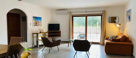 Ein modernes Wohnzimmer mit einem Flachbildfernseher, zwei Sesseln, einer Couch und einem Essbereich mit einem Marmortisch.