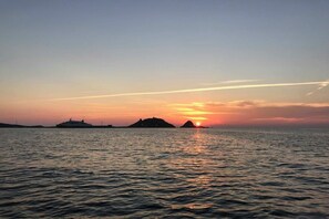 Solnedgang over stille vand med et skib og to øer i horisonten.