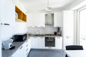 A modern kitchen with white cabinets, a built-in microwave, a gas stove, and a sink. - Domus Rubina - terrace sea view (Sorrento)