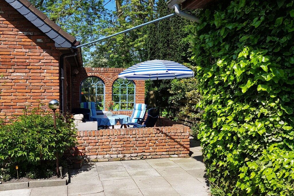 Un bâtiment en briques doté d’un patio comprenant une table et des chaises, un parasol et un mur en briques.