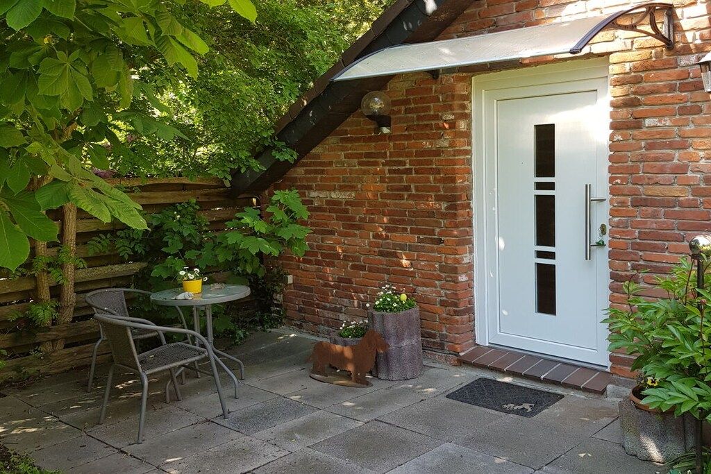 A brick house with a white door, a small patio with a table and chairs, and potted plants.
