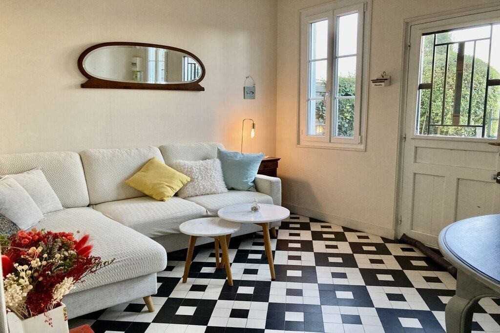 A room with a checkered floor, a white sofa with cushions, a round table, and a mirror on the wall.