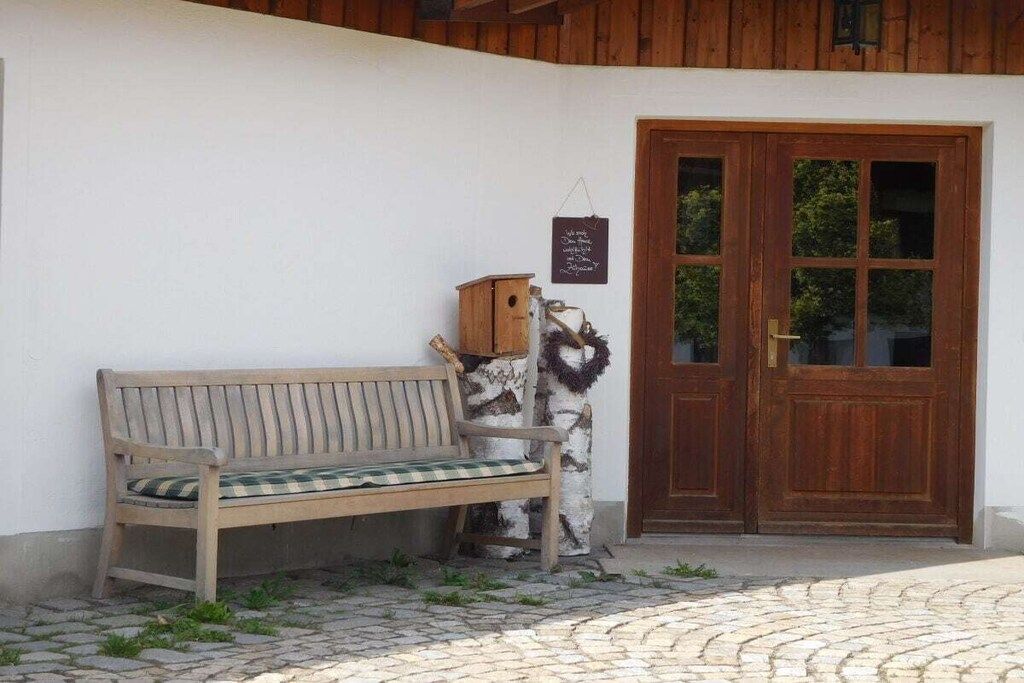 A wooden bench with a checkered cushion outside a building with a wooden door and a wall-mounted sign.