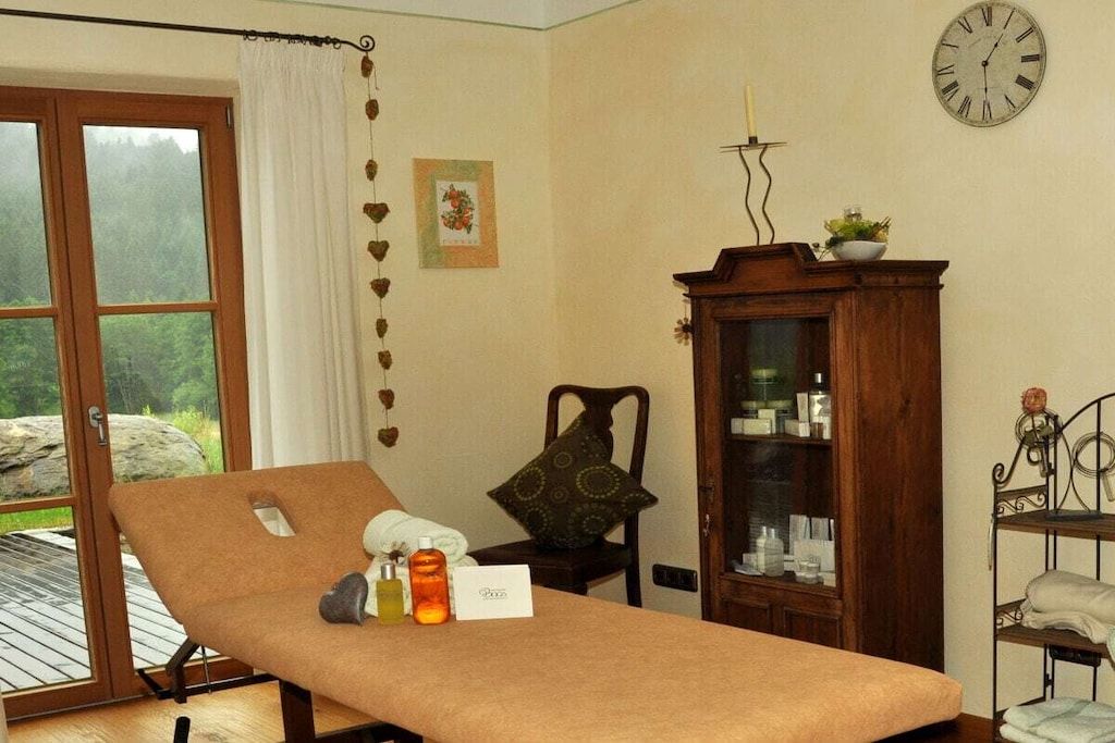 A room with a massage table, a cabinet with bottles, a chair, and a clock on the wall.