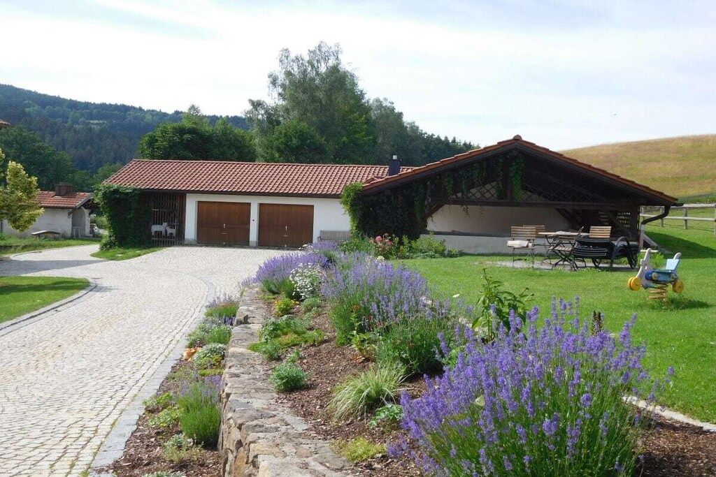 A rural property with a paved driveway, a garage, and a covered outdoor seating area with a table and chairs.