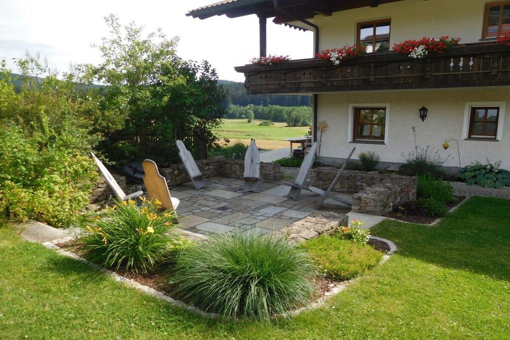 A house with a stone patio, outdoor seating, and a garden with various plants.