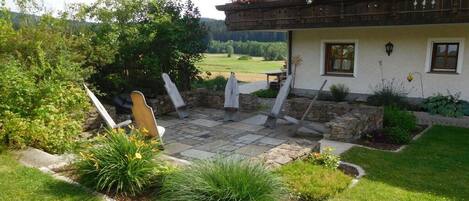 A house with a stone patio, outdoor seating, and a garden with various plants.