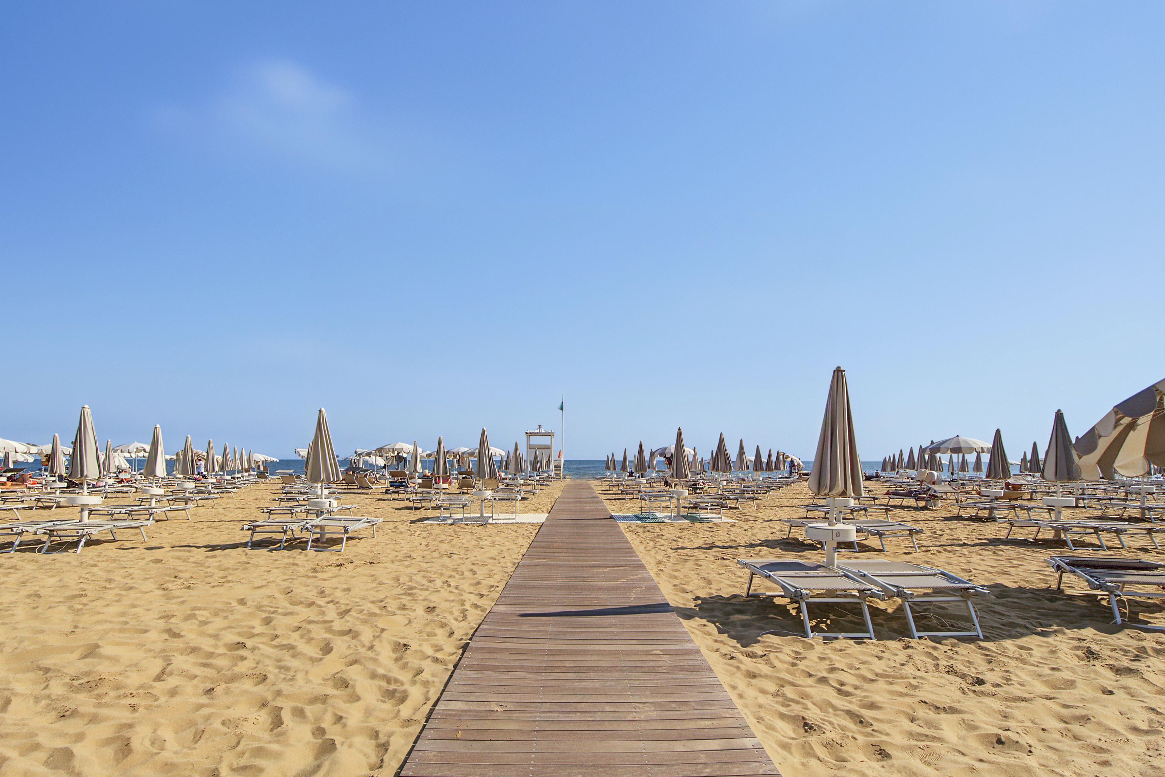 Una spiaggia con una passerella in legno che conduce al mare, fiancheggiata da lettini e ombrelloni.