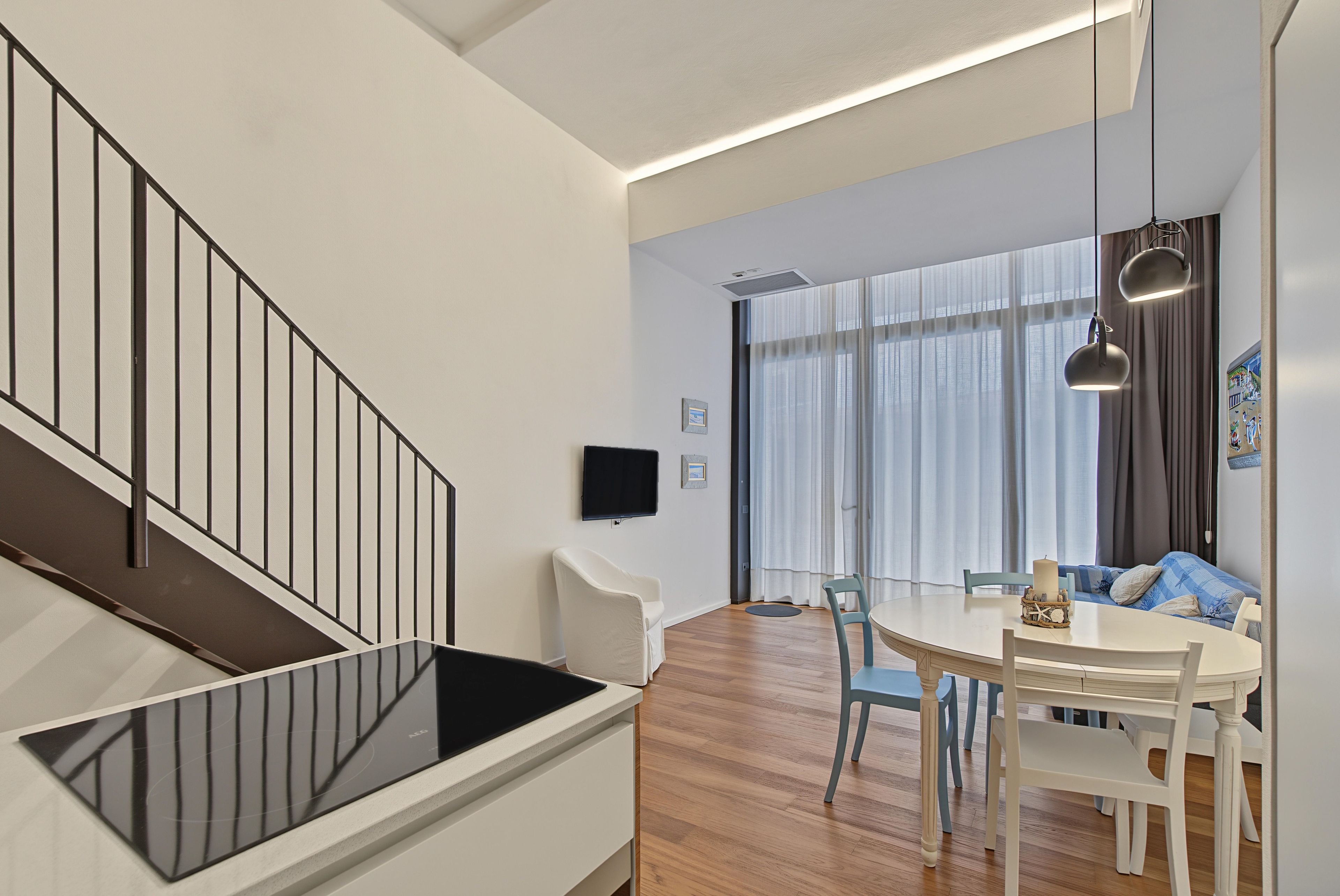 A modern interior with a staircase, a dining area, and a living space with a sofa and a TV.