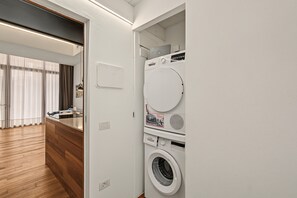 Un lavadero con lavadoras y secadoras apiladas, piso de madera y pared blanca.