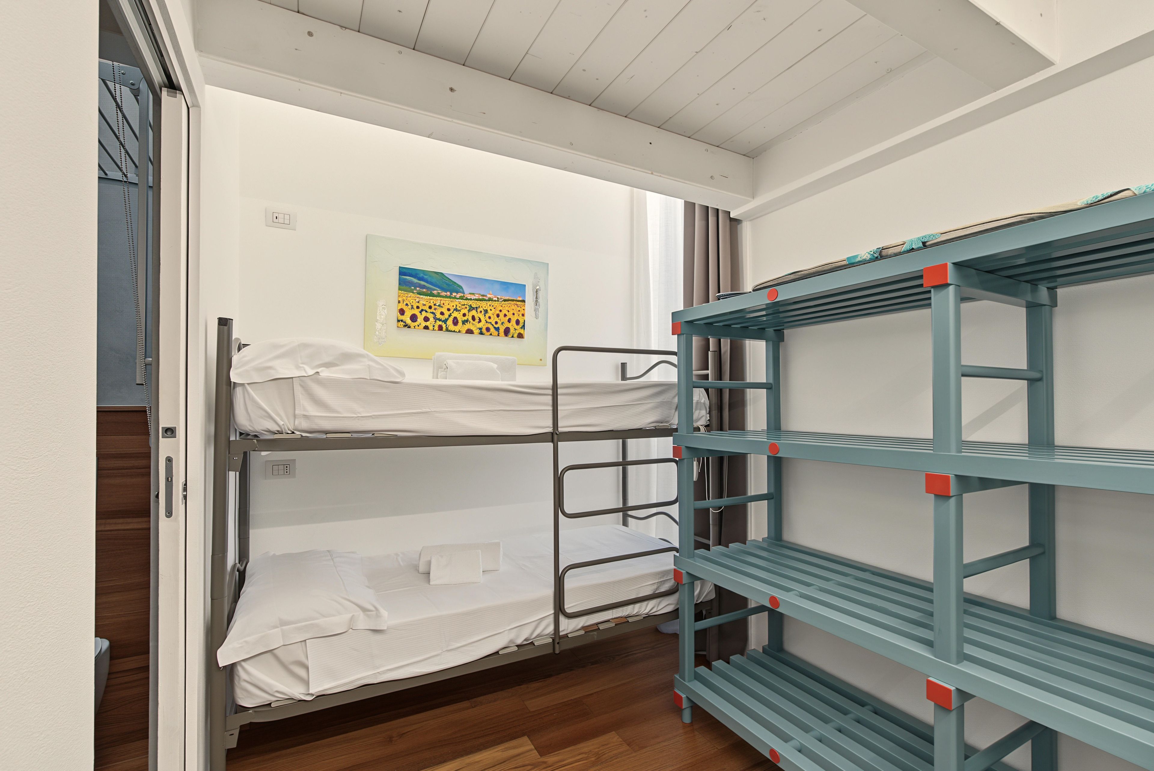 A bunk bed room with a painting on the wall and a blue metal shelf unit.