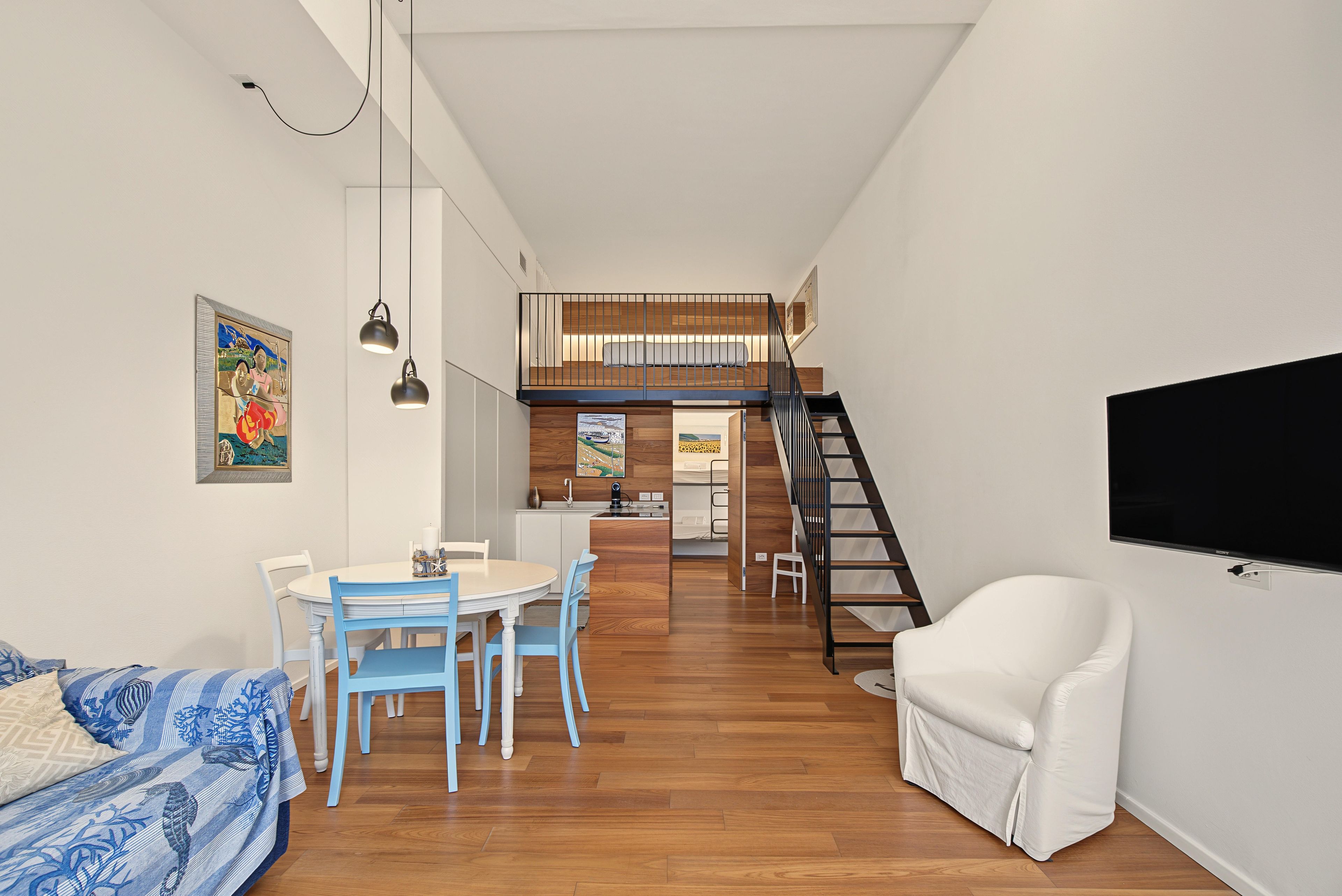 Un interno moderno con zona pranzo, una divano, una poltrona bianca e una scala che conduce a una mansarda.