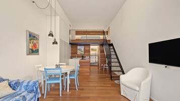 Un interno moderno con zona pranzo, una divano, una poltrona bianca e una scala che conduce a una mansarda.